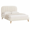 Cama tapizada de tela beige con cabecera curva y patas de madera